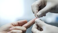 Medical professional in white gloves performing blood glucose test on patient finger using lancet device for diabetes monitoring and healthcare diagnosis.