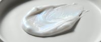 Creamy white cosmetic product smear with pearlescent shimmer on neutral background, suitable for skincare, beauty, and cosmetics marketing materials.