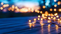 Glowing fairy lights on wooden deck at dusk create magical ambiance with blurred bokeh city lights in background, capturing cozy outdoor evening atmosphere.