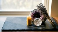 Spiritual wellness setup with healing crystals, burning candle, dried lavender bundle and crystal sphere on dark slate surface for meditation and relaxation.