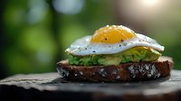 Gourmet open sandwich with sunny side up egg and fresh avocado on dark rustic bread, served on wooden surface against blurred natural background.