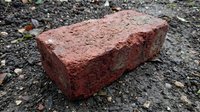 Old weathered red brick lying on gravel ground showing texture and wear from age and elements for construction and building material concepts.