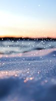 Sparkling snow crystals glisten against sunset sky, creating magical winter atmosphere with bokeh effect and soft pastel colors on frozen landscape at dusk.