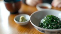 Fresh seaweed salad with sesame seeds in ceramic bowl on wooden table, accompanied by wasabi and soy sauce for Japanese dining experience.