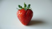 Fresh ripe strawberry with green leaves on white background, showcasing vibrant red color and natural texture for food photography and healthy eating concepts.
