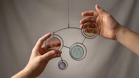 Hands reaching for hanging circular metal rings in balanced mobile sculpture representing connection, teamwork and coordination in minimalist setting.