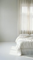Minimalist bedroom corner with unmade white bed and sheer curtains filtering natural light creating serene morning atmosphere for interior design.