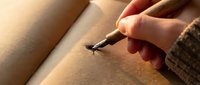 Artist's hand holding brush while painting on canvas with warm natural lighting during creative work session.
