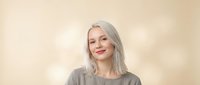 Young blonde woman smiling warmly in casual gray sweater against soft beige background for lifestyle and portrait photography projects.