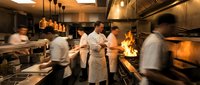 Busy professional kitchen with chefs cooking during dinner rush. Motion blur captures fast-paced restaurant service with flames and stainless steel equipment.