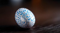 White Easter egg decorated with blue floral folk art pattern on dark wooden background, traditional seasonal design for spring holiday celebration.
