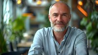 Portrait of confident mature Caucasian businessman with gray beard wearing casual shirt, sitting in modern cozy cafe. Perfect for business, leadership, and success concepts.