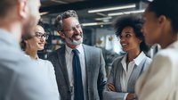 Diverse business team engaged in positive conversation during office meeting, showcasing collaboration and professional networking in corporate environment.
