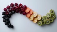 Fresh berries and fruits arranged in rainbow curve pattern with blackberries, raspberries, strawberries, bananas and kiwi slices on gray background. Food art composition.