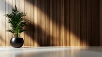 Green palm plant in black round pot against wooden wall with dramatic diagonal sunlight and shadows on minimalist interior background.