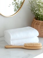 Minimalist bathroom setting with white fluffy towels, wooden massage brush, round mirror and wicker basket with baby breath flowers on marble counter.