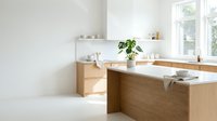 Modern minimalist bathroom with light wood cabinetry, white countertops, and potted plant. Bright natural light from windows creates clean, contemporary spa-like atmosphere for home design and interior decoration projects.