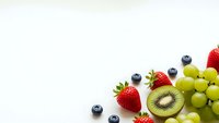Fresh mixed fruits arrangement with strawberries, blueberries, kiwi slices and green grapes on white background for healthy eating and nutrition concepts.