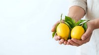 Fresh yellow lemons with green leaves held in hands against white background, suitable for food, agriculture, and healthy lifestyle marketing materials.