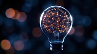 Glowing light bulb filled with illuminated copper wire stars and sparkles against dark background with bokeh lights creates magical atmosphere.
