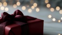 Elegant burgundy gift box with satin bow against blurred bokeh lights background, creating romantic holiday atmosphere for special occasions.