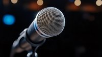 Professional dynamic microphone on dark background with bokeh lights, close-up view showing detailed metal mesh grille. Music and audio recording concept.