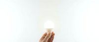 Hand holding glowing light bulb against white background symbolizing innovation creativity and bright ideas for business concepts.