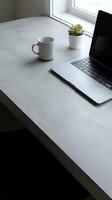 Minimalist home office workspace with laptop, coffee mug and succulent plant on concrete desk by window for remote work and productivity.