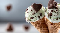 Mint chocolate chip ice cream scoops in waffle cone topped with heart-shaped chocolate decorations against blurred background, sweet dessert macro photography.