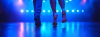 Feet of dancers on stage with dramatic blue lighting and bokeh effects creating atmospheric performance ambiance, low angle panoramic view.
