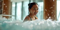 Young Asian woman smiling in swimming pool with splashing water, enjoying wellness spa relaxation during vacation or weekend getaway.