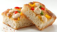 Freshly baked focaccia bread topped with colorful bell peppers, chicken chunks, and creamy sauce on white background, showcasing Italian cuisine.