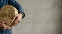 Mature man with weathered hands holding fresh whole grain bread loaf against neutral background, suitable for bakery, food, nutrition and culinary content.