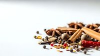 Aromatic spices and seasonings scattered on white background including cinnamon sticks, star anise, peppercorns and dried chili for culinary cooking.