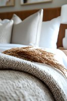 Cozy bedroom setting with dried wheat stalks on knitted blanket against white pillows, creating rustic farmhouse atmosphere for interior design and home decor styling.