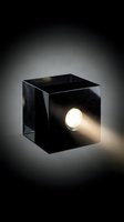 Modern black cubic light fixture with glowing warm LED bulb emitting bright beam against neutral background. Minimalist design element for contemporary interior, architectural visualization, and lighting product showcase.