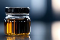 Glass jar with golden amber liquid on reflective surface against dark blue background, dramatic lighting highlights ribbed texture and transparency.