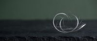Transparent glass sphere with swirling light trails on dark textured surface, isolated on neutral background for design projects.