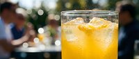 Refreshing iced orange juice in a glass with ice cubes, outdoor cafe setting, blurred people in background, sunny day.