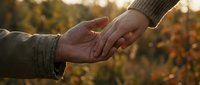 Two hands reaching toward each other in warm golden sunlight with autumn foliage background, symbolizing connection, support, and human compassion in nature.