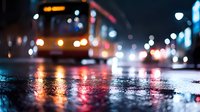 Blurred city bus driving through wet street at night with colorful light reflections on asphalt pavement creating atmospheric urban transportation scene.