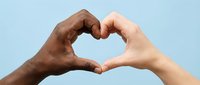 Two diverse hands forming a heart shape together on a light blue background, symbolizing unity, love, and racial harmony.