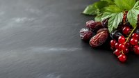 Fresh red currant berries and dried dates on dark stone background with green leaves, copy space for text. Natural healthy organic food concept.