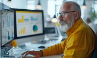 Senior businessman with white beard analyzing financial data on computer screens with colorful charts and graphs in modern office environment.