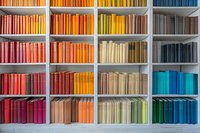Colorful books arranged by spectrum on white shelves creating rainbow pattern. Books organized from red through orange, yellow, and blue tones for modern library design.