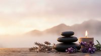 Zen spa stones balanced with burning candle and lavender flowers on wooden surface against mountain lake sunset background for meditation relaxation.