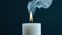 White candle with glowing flame and elegant smoke trail rising against dark blue background, creating atmospheric mood for meditation or remembrance.