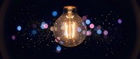 Glowing vintage Edison bulb with warm filament against dark starry background with colorful bokeh lights for creative design projects.