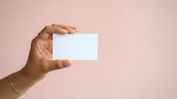 Hand holding blank white business card against soft pink background, isolated for branding and corporate design mockups.