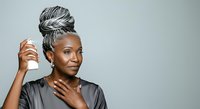 Mature African American woman with gray braided hair styled in updo, wearing dark shirt, touching face and neck against neutral background.